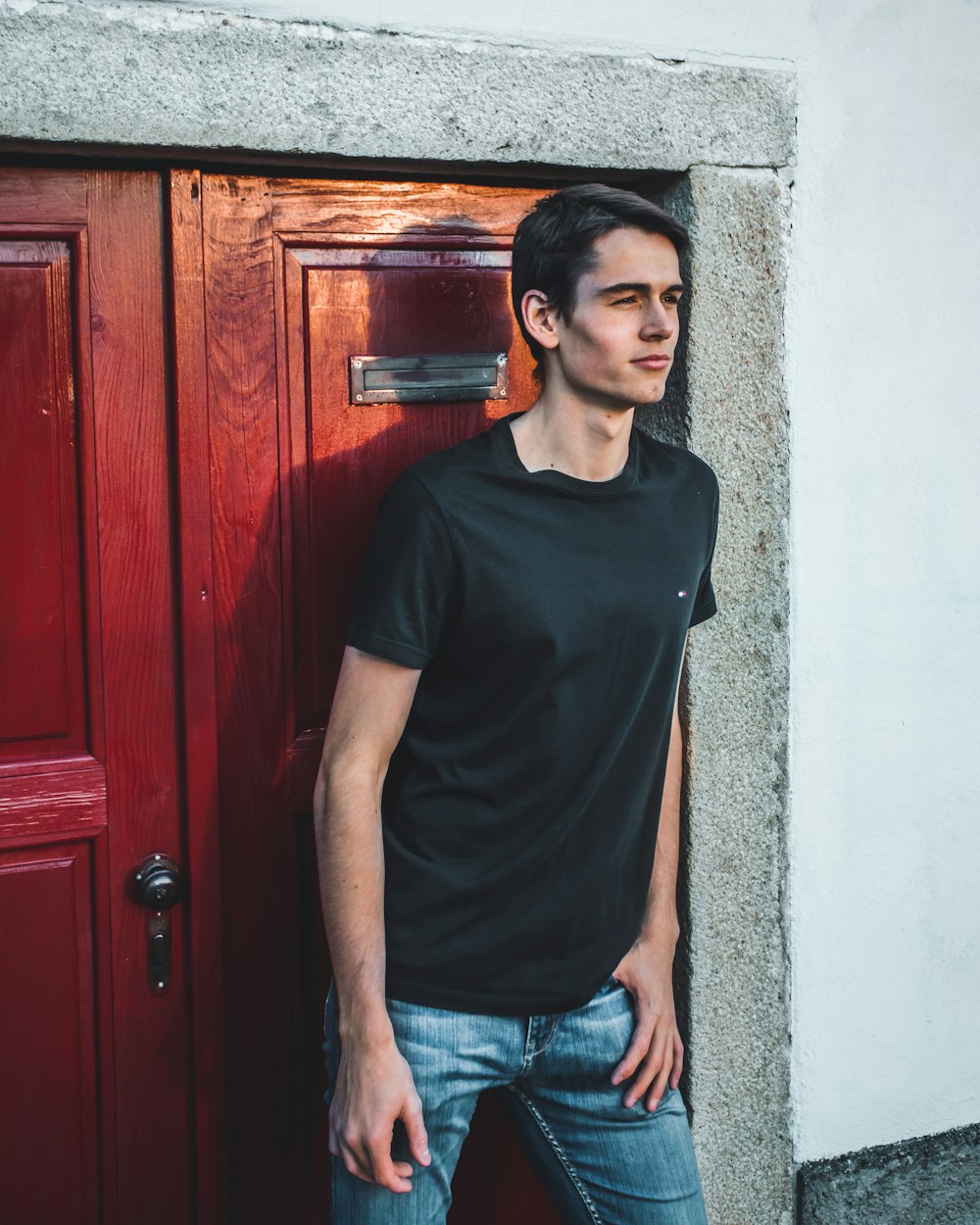 uomo in t-shirt girocollo marrone e jeans blu in denim in piedi accanto alla porta di legno marrone