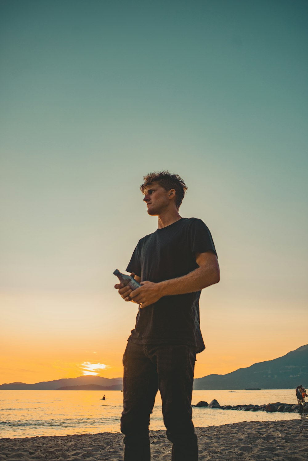 man in black crew neck t-shirt holding black smartphone during sunset