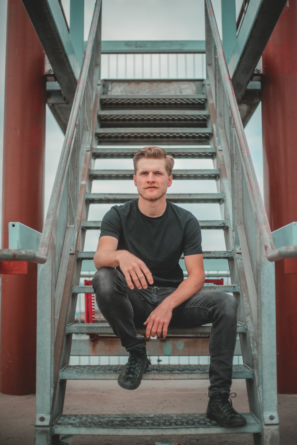 man in black crew neck t-shirt sitting on black metal staircase