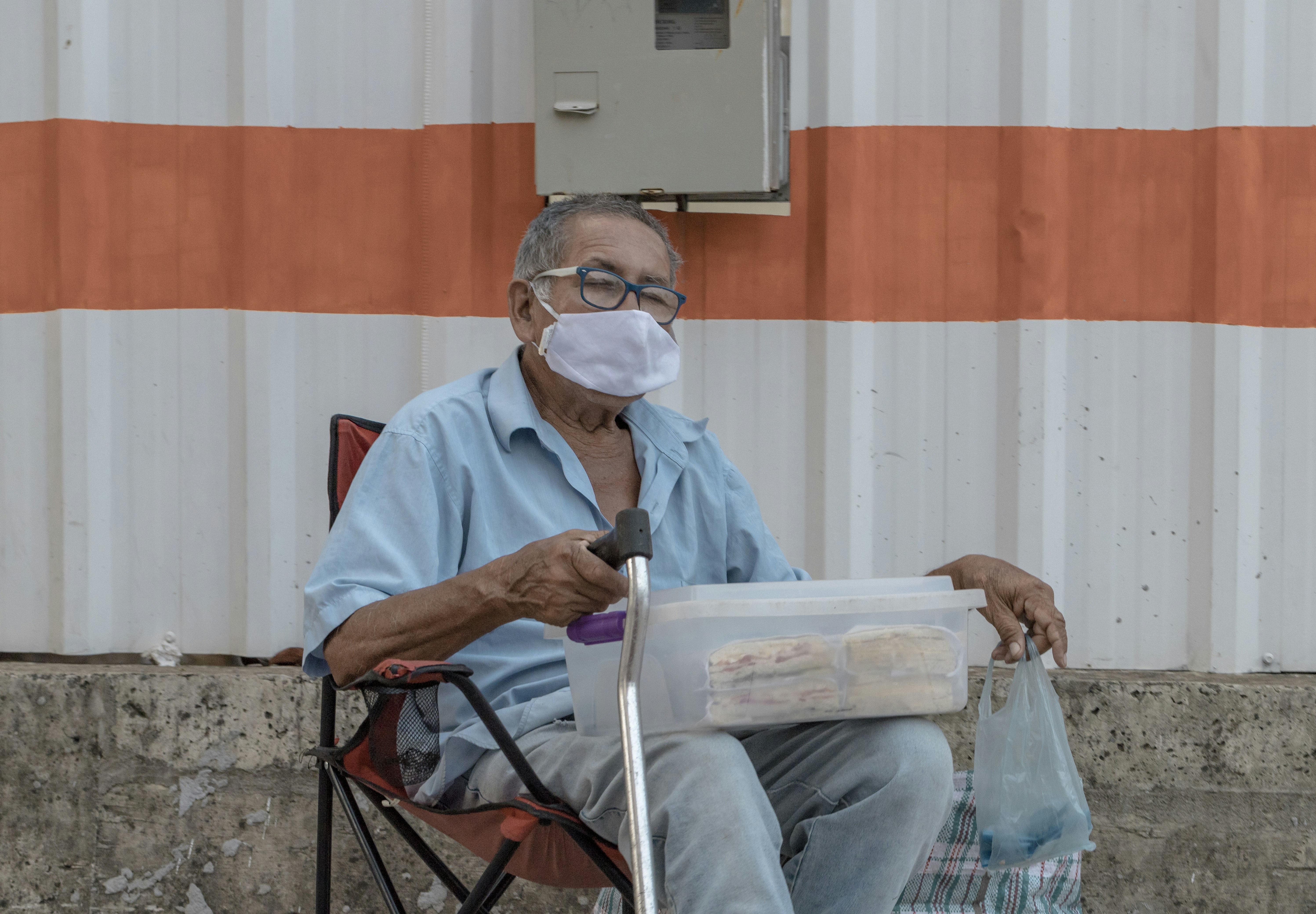 man in blue button up shirt sitting on red and black folding chair reading newspaper