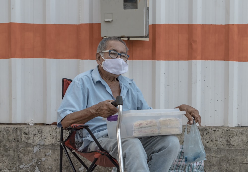 hombre con camisa azul abotonada sentado en una silla plegable roja y negra leyendo el periódico