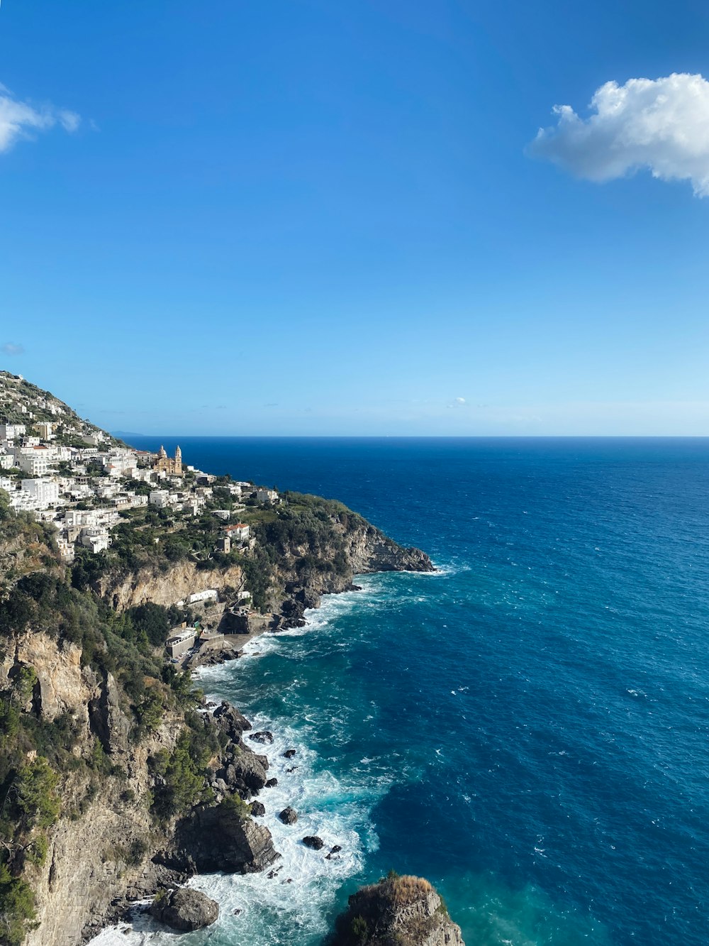 montagna verde e marrone accanto al mare blu sotto il cielo blu durante il giorno