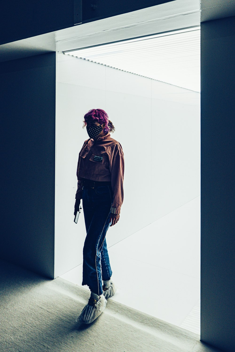 woman in brown jacket and blue denim jeans standing on white floor tiles