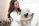 Photo of a smiling woman holding a matte white ceramic vase in a cozy living room.
