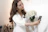 Photo of a smiling woman holding a matte white ceramic vase in a cozy living room.