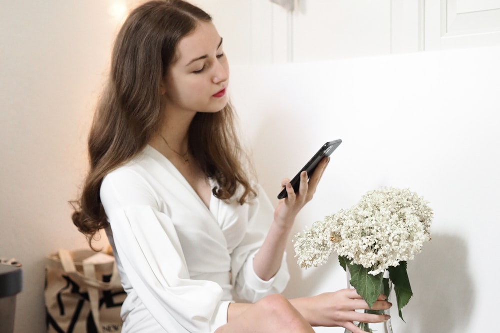 woman in white dress shirt holding smartphone