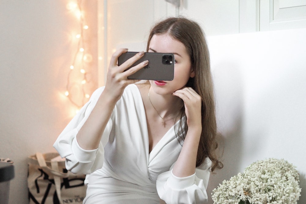 woman in white long sleeve shirt holding black smartphone