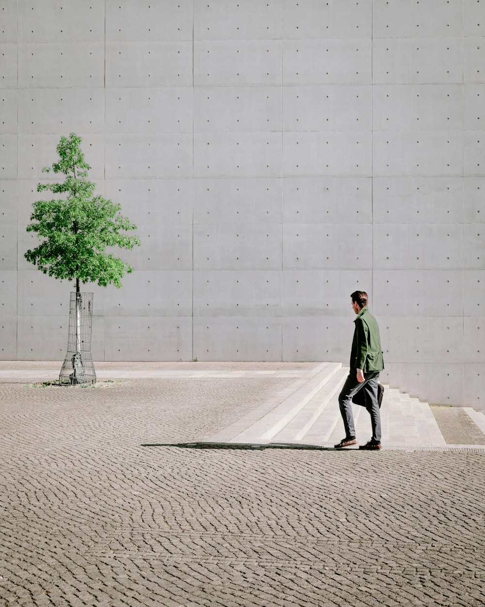 femme en manteau vert marchant sur le trottoir en béton gris