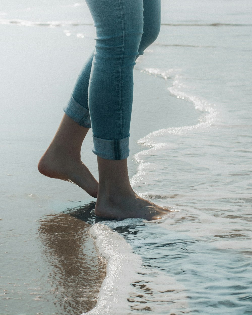 Person in blauen Jeans, die tagsüber am Strandufer steht