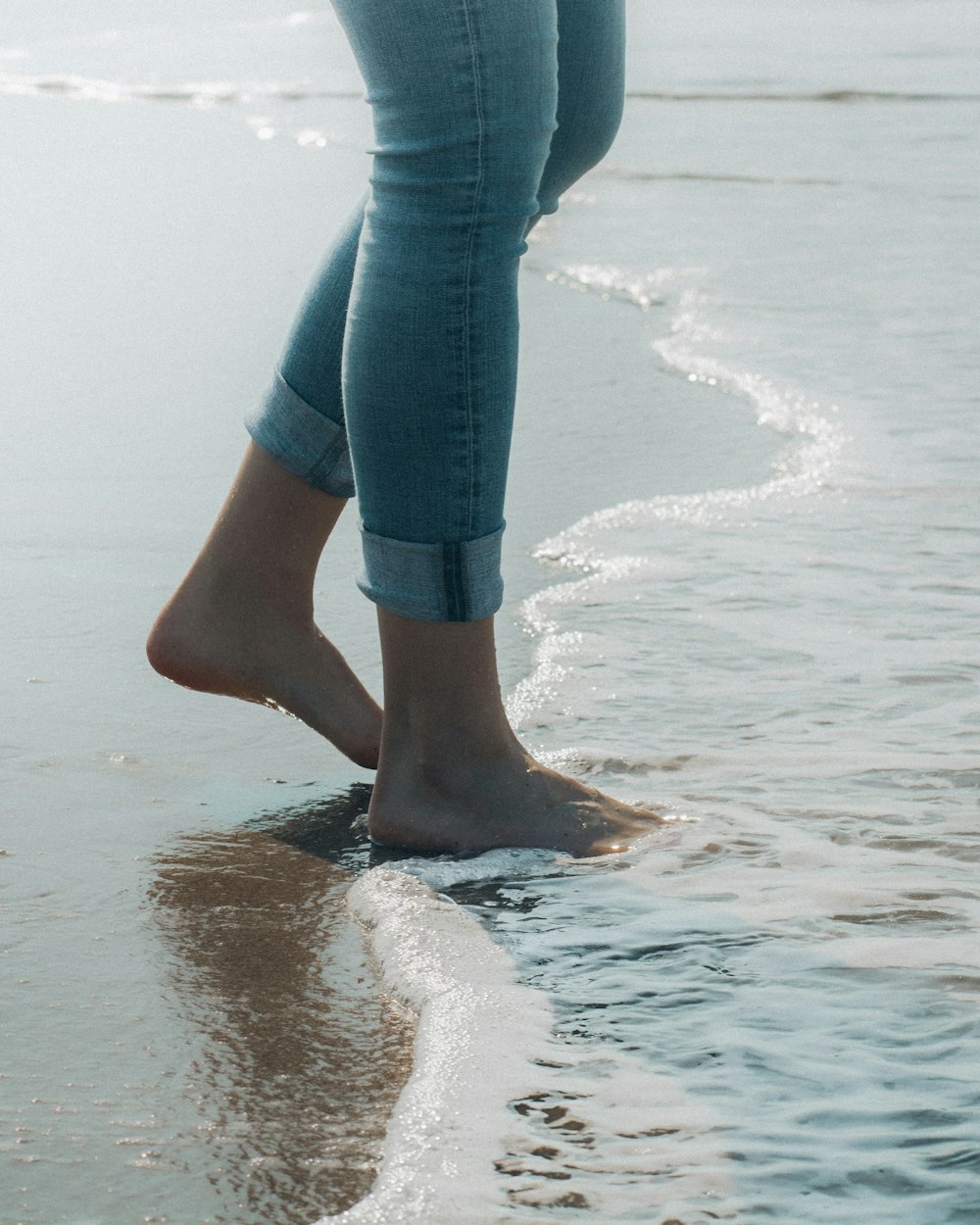Persona con jeans de mezclilla azul de pie en la orilla de la playa durante el día
