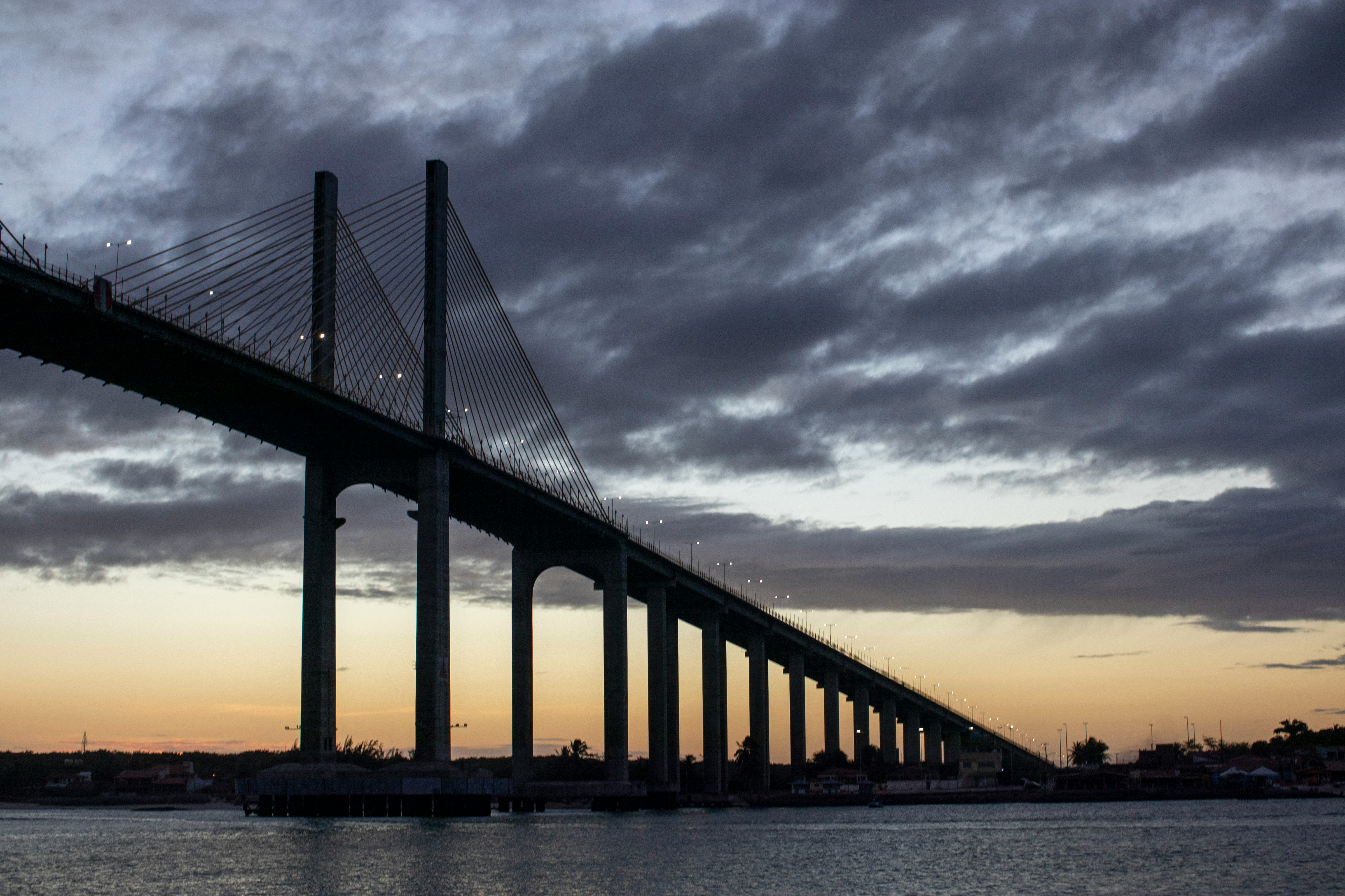 silhouette of bridge under cloudy sky during sunset