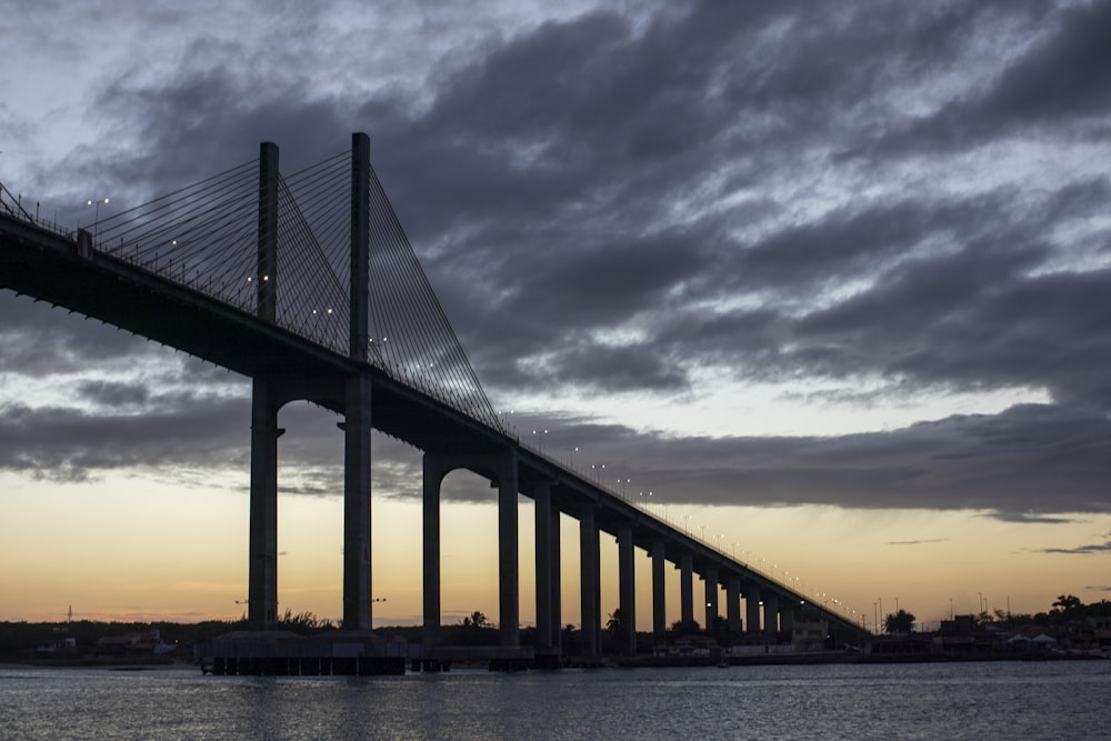 silhouette of bridge under cloudy sky during sunset