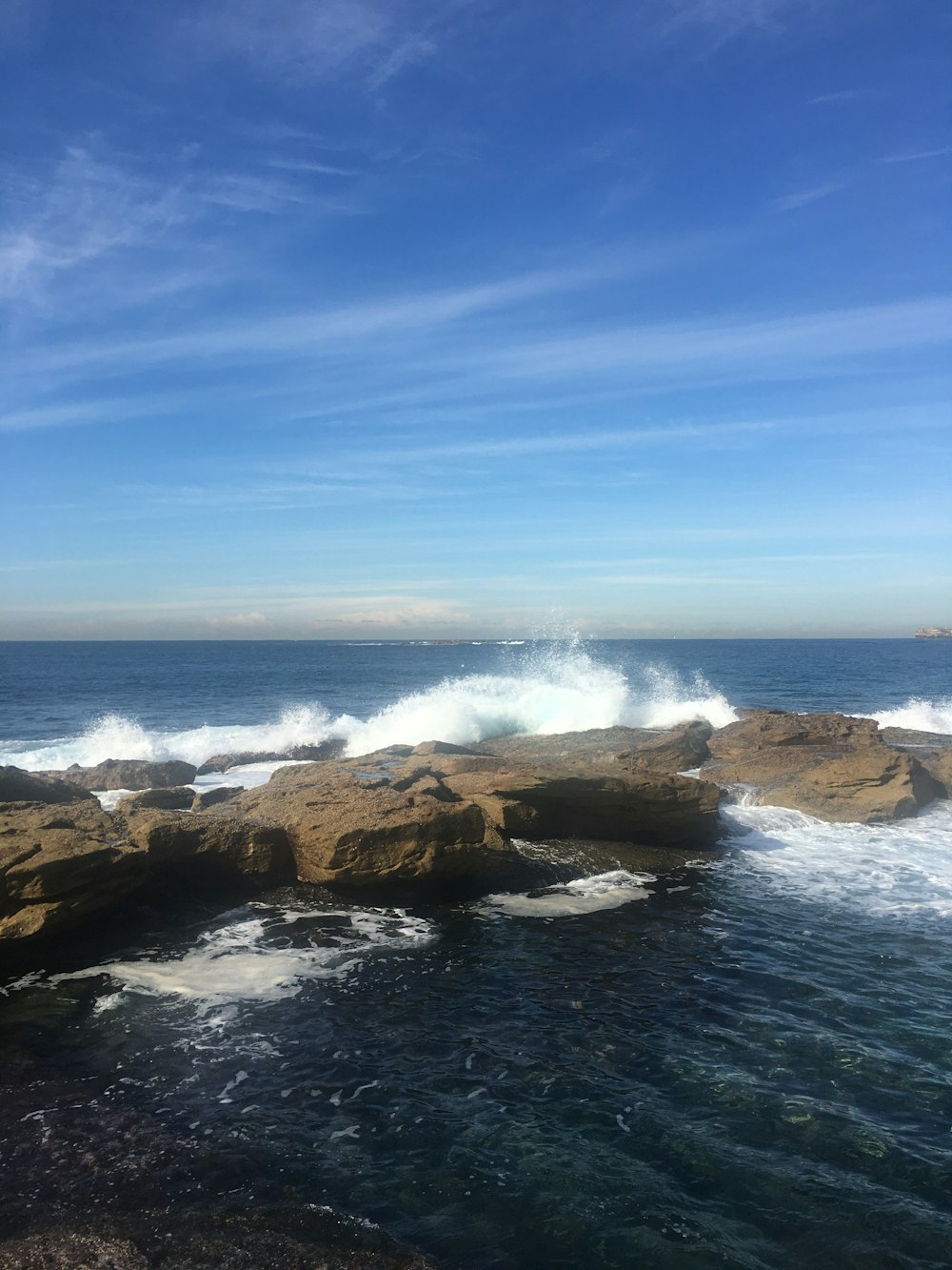 ocean waves crashing on brown rocky shore under blue sky during daytime