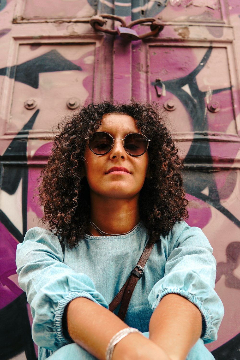 a woman wearing sunglasses sitting in front of a graffiti covered wall