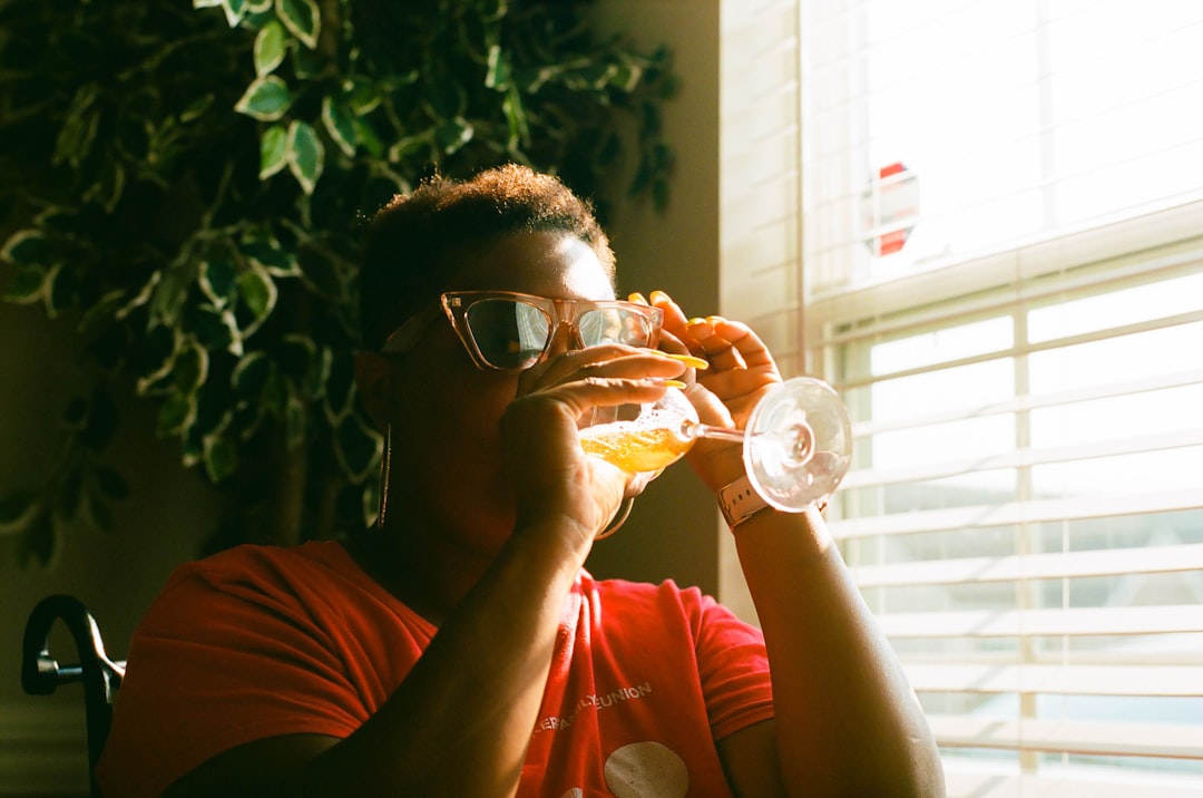 man in red crew neck t-shirt wearing black framed eyeglasses holding clear drinking glass