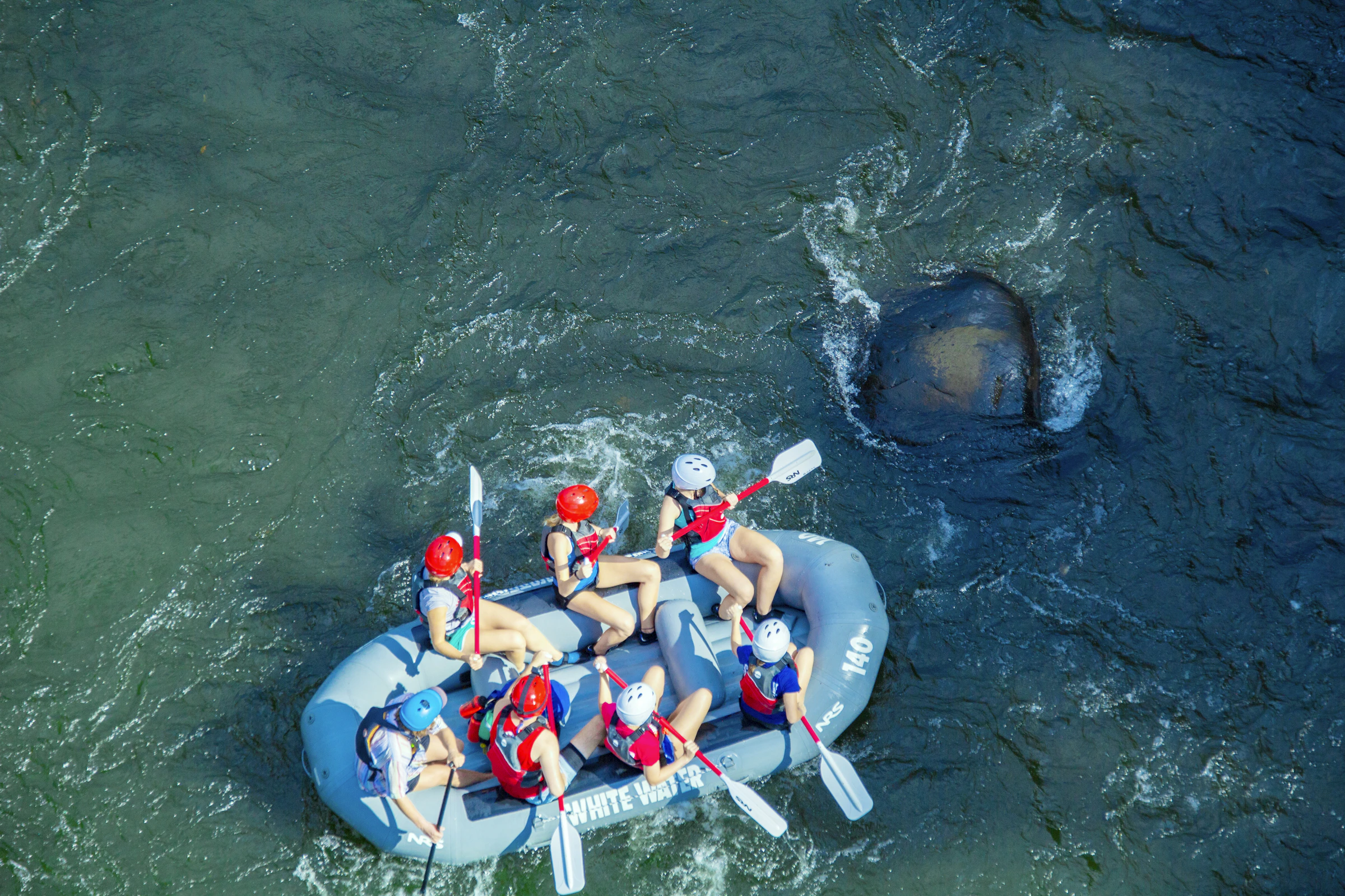 A rafting team wearing helmets and life vests on moving river water