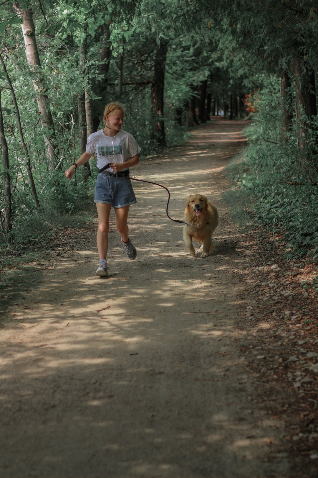 woman in blue t-shirt and blue denim shorts walking with brown dog on pathway during