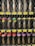 A neatly organized display of black spray paint cans is behind a wire fence. Each can is labeled with the word 'BLACK' in large text, and they are aligned in rows on shelves. Energy and vibrancy are added by colorful caps in shades of red, purple, and yellow. Price tags are visible below each row.