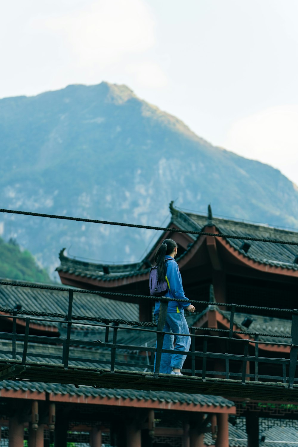 woman in blue long sleeve shirt and blue denim jeans standing on brown wooden bridge during