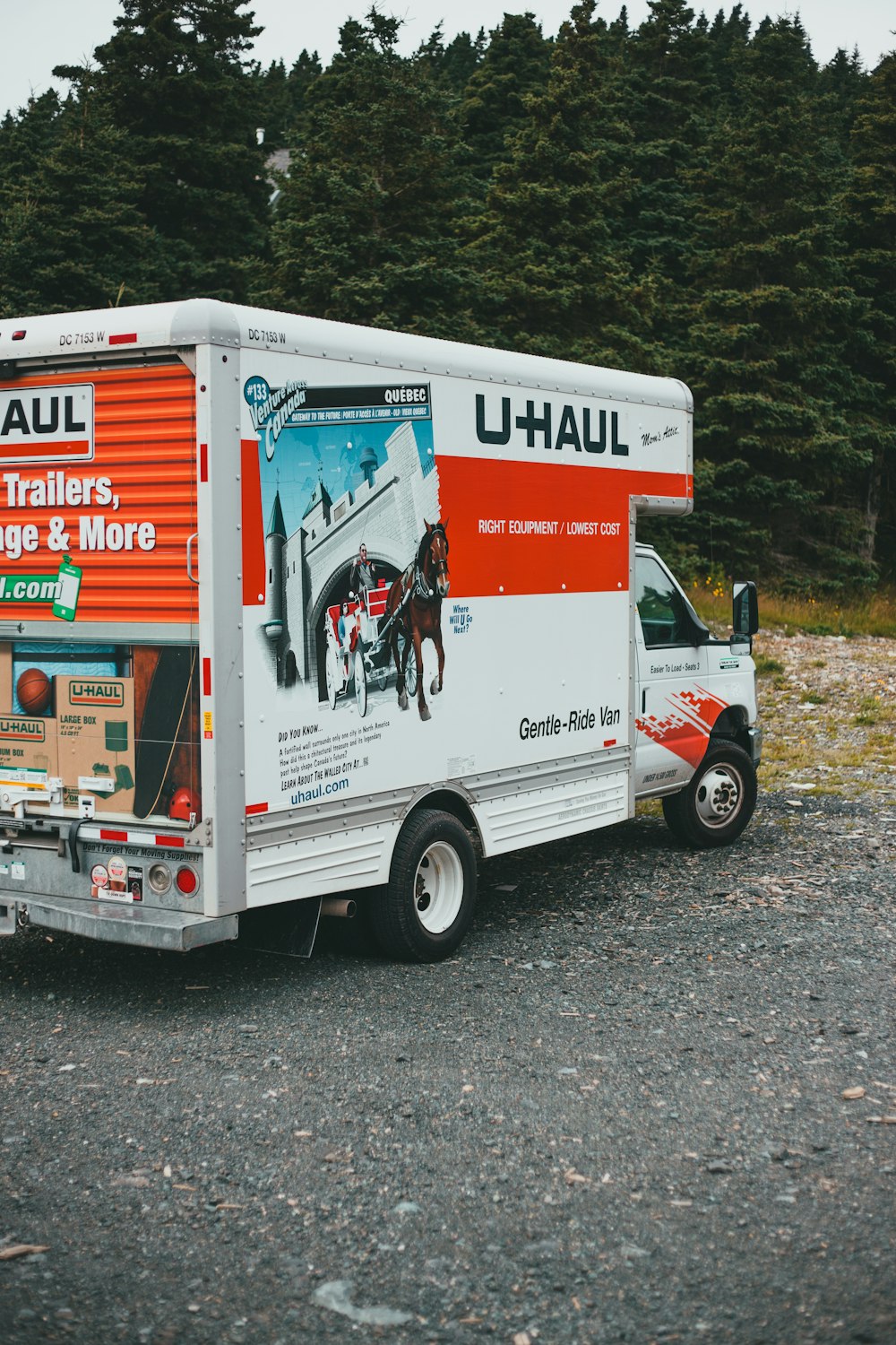 a moving truck parked in a gravel lot with trees in the background