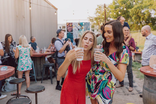 A lively outdoor gathering of women sharing stories and laughter under string lights at dusk.