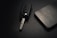 A car key with an extended metal blade is placed next to a modern smartphone on a dark textured surface. The lighting is subtle, creating a sleek and minimalistic aesthetic.