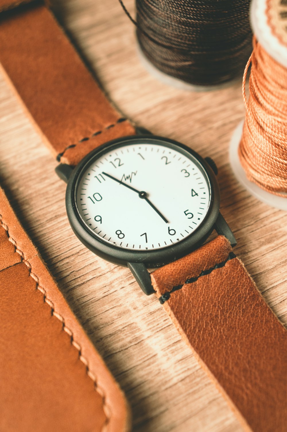 a watch sitting on top of a table next to a spool of thread