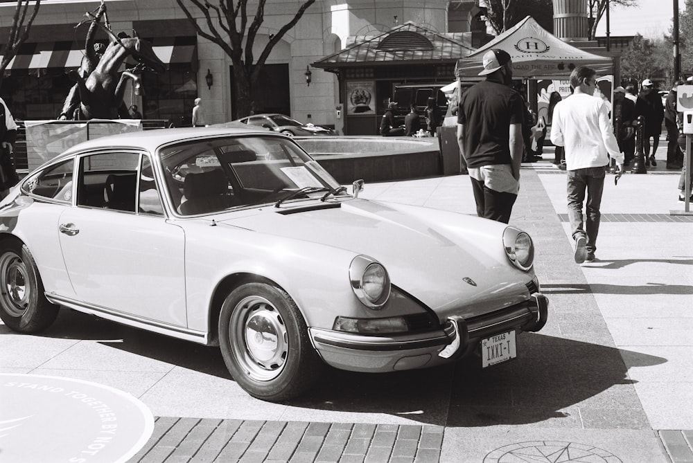 grayscale photo of man in black suit standing beside classic car