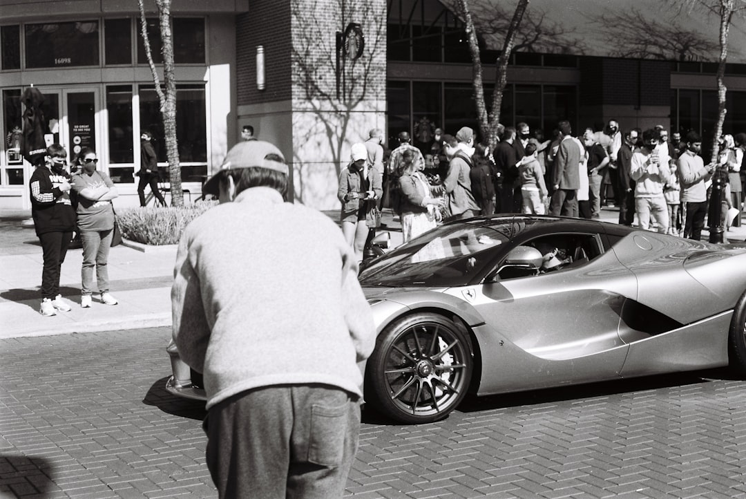 man in white long sleeve shirt and gray pants standing beside black coupe
