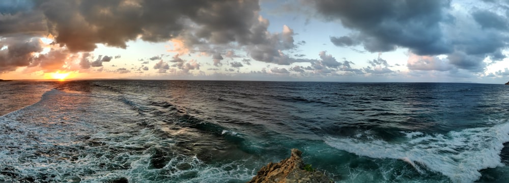 Meereswellen, die tagsüber unter weißen Wolken und blauem Himmel auf braune Felsformationen stürzen