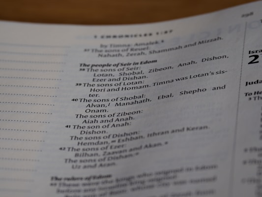 A close-up view of a page from a book, specifically a Biblical text. The text is organized into numbered sections, listing the genealogy of people from the region of Edom. The text includes various names such as Lotan, Shobal, and Alvan. The headings and sections are printed in distinguishable fonts, emphasizing hierarchy in the content.