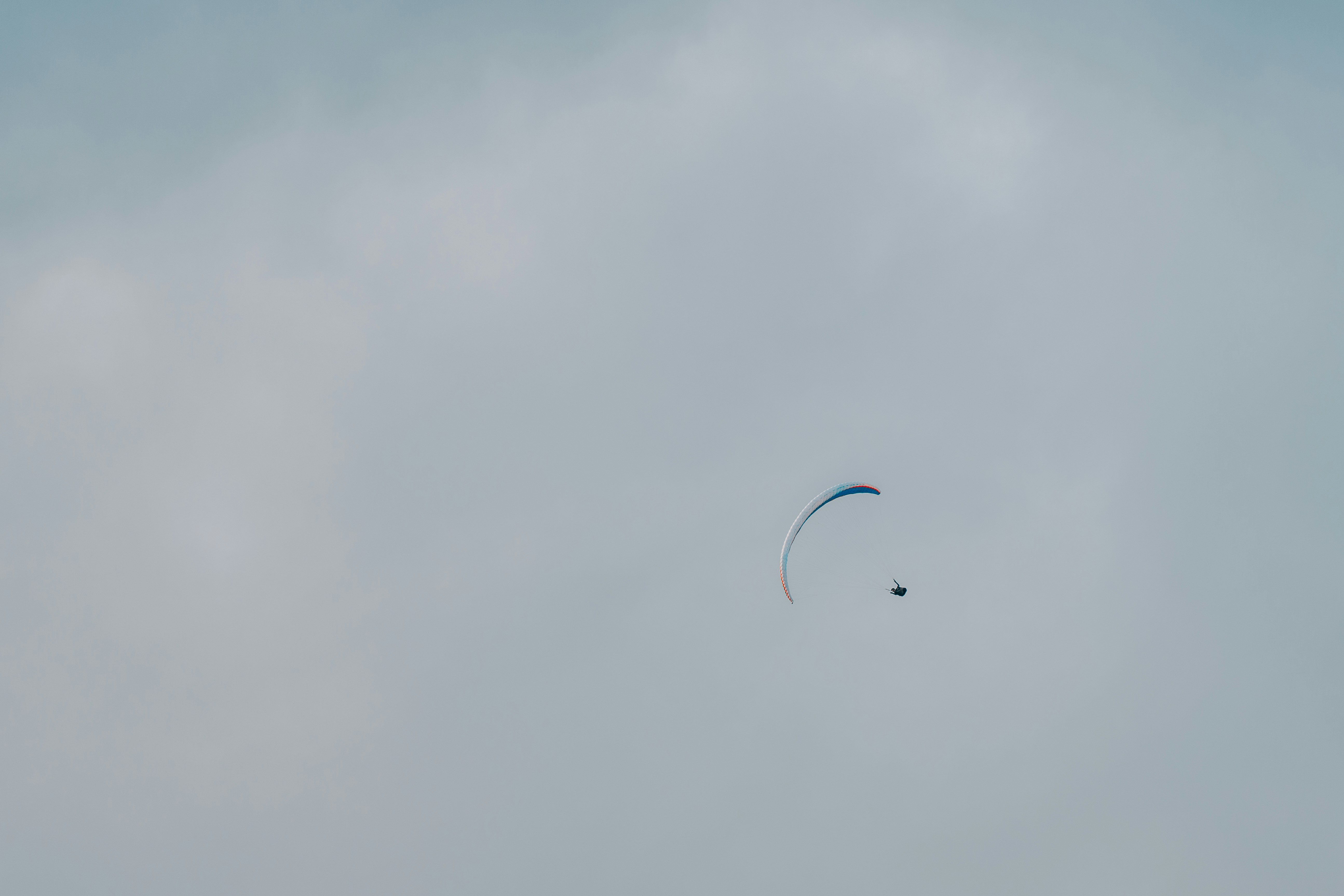 person in white shirt with blue parachute in the sky