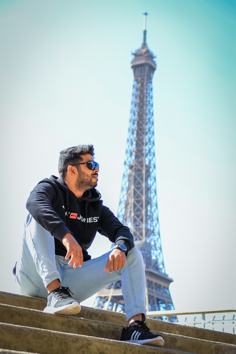 man in black and white hoodie and blue denim jeans sitting on concrete wall during daytime