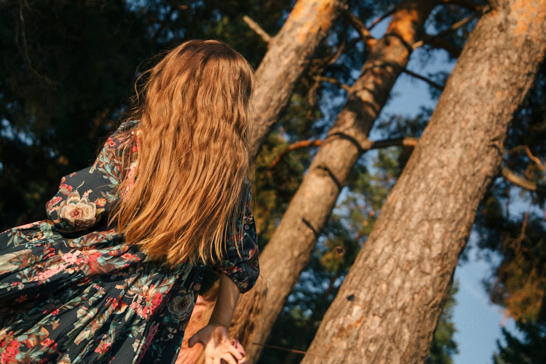 woman in black red and white floral dress standing near brown tree during daytime