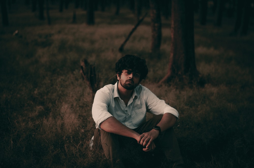 man in white polo shirt sitting on brown grass