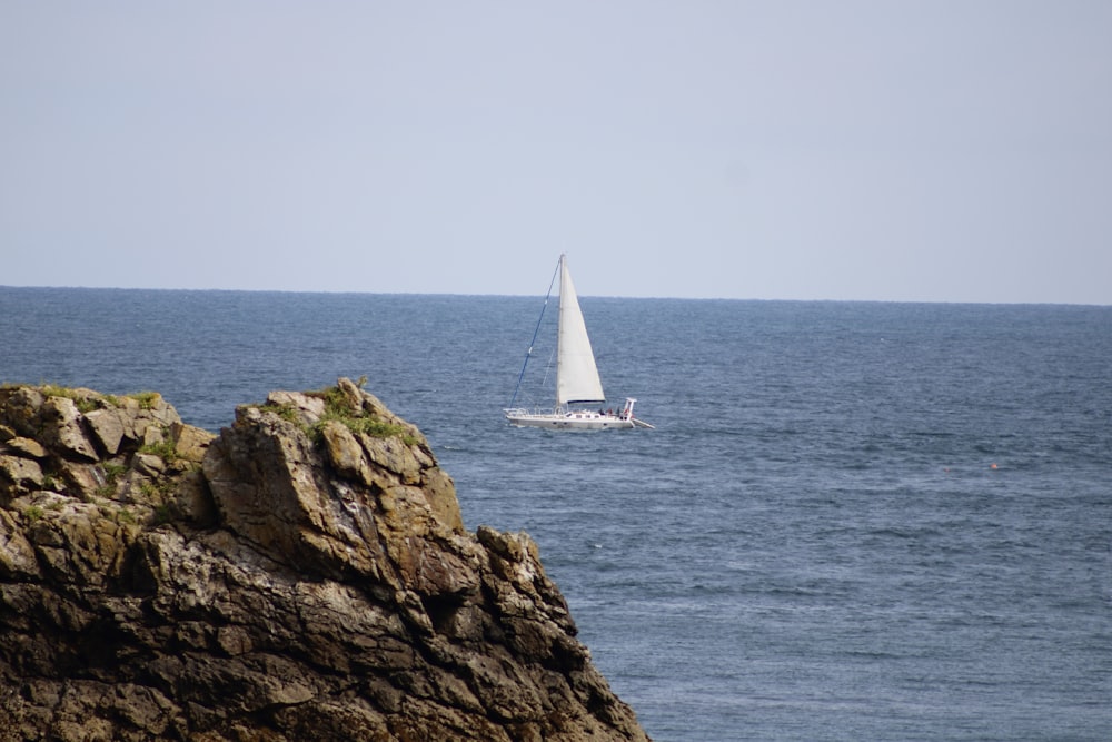 barca a vela bianca sul mare vicino alla formazione rocciosa marrone durante il giorno
