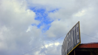A large sign with the word 'RISTORANTE' is positioned at the top of a building against a backdrop of a partly cloudy sky. The clouds are thick and white, with patches of bright blue sky peeking through.