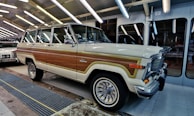 A classic cream and wood-panelled SUV is parked in a well-lit garage or automotive facility. The vehicle features chrome accents and retro-style wheels, with another classic car visible partially in the background.