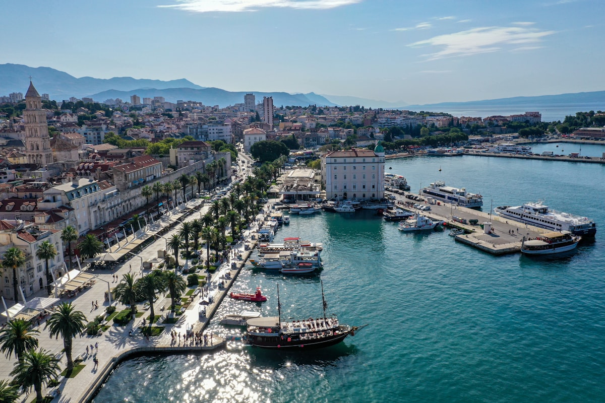 Split July — a red and white boat on the Split harbour with the cathedral bell tower and palm-lined Riva behind, peak summer