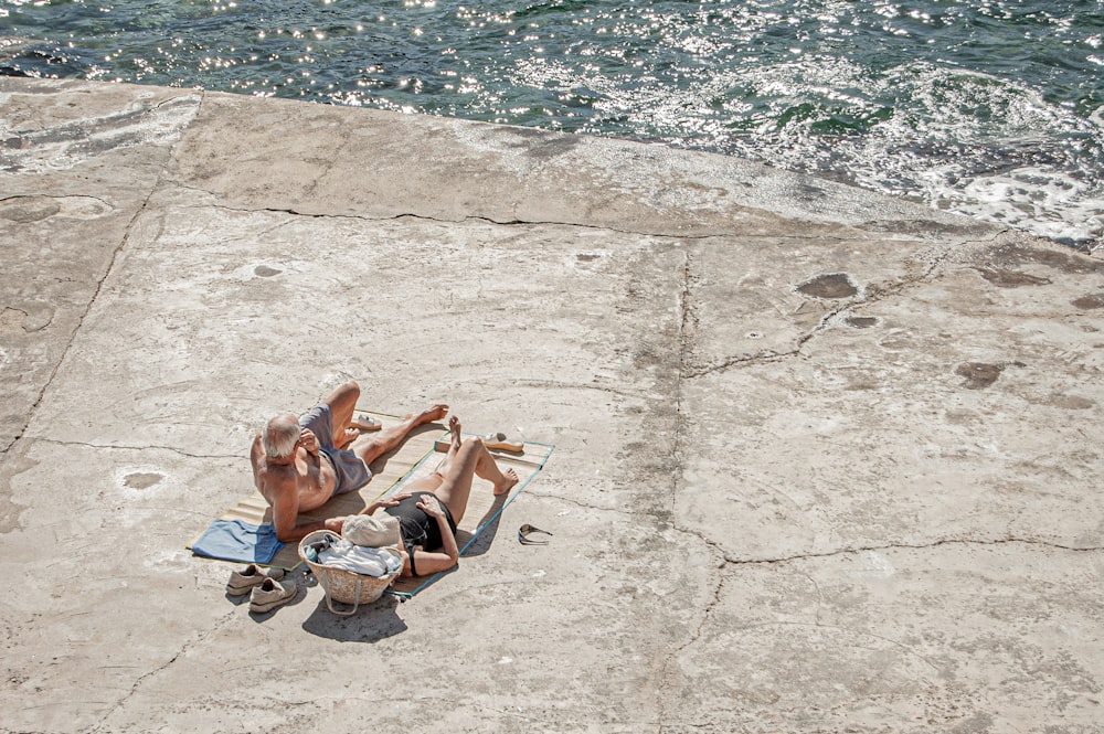 2 women lying on concrete floor near body of water during daytime