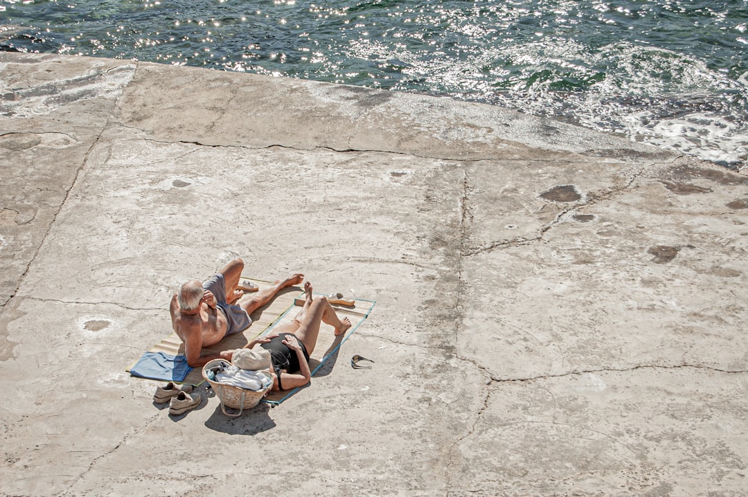 2 women lying on concrete floor near body of water during daytime