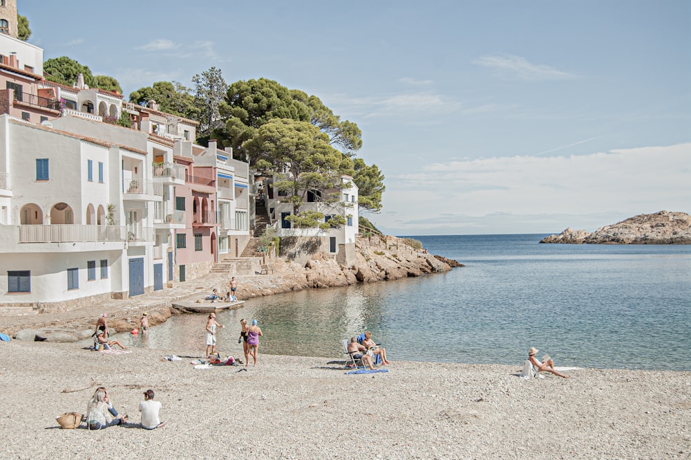 a group of people sitting on a beach next to a body of water