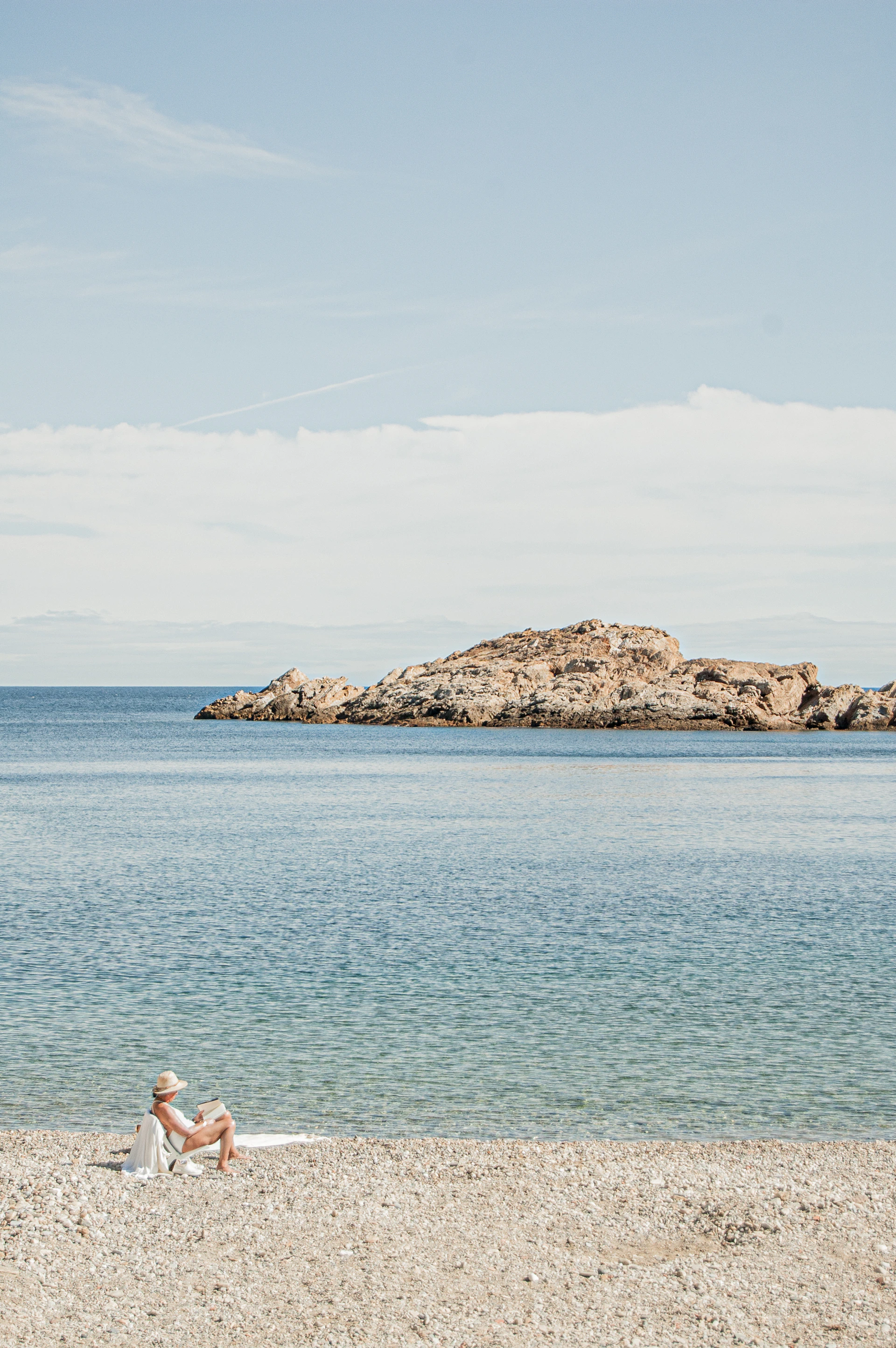 woman in white shirt sitting on rock formation near body of water during daytime
