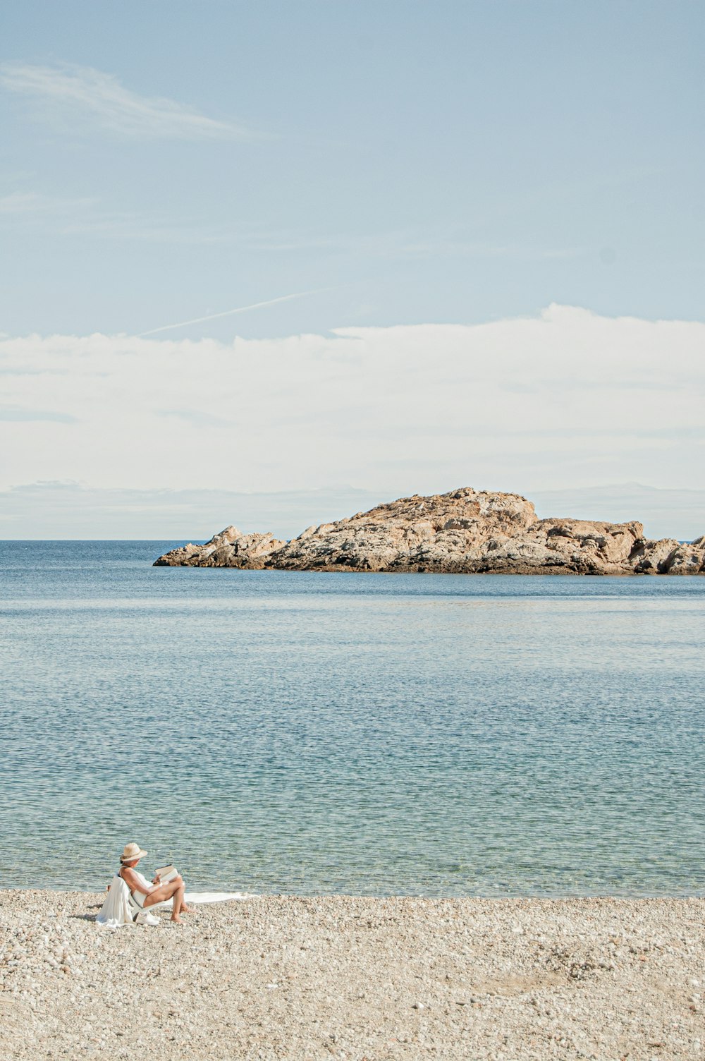 woman in white shirt sitting on rock formation near body of water during daytime