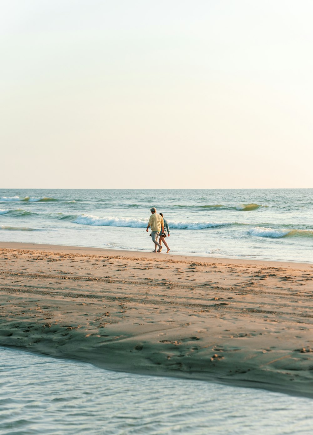 흰 셔츠와 검은 바지를 입은 남자가 낮 동안 해변을 걷고 있다
