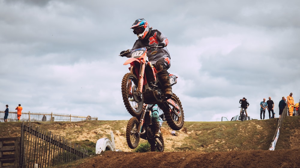 man in red and black motorcycle suit riding motocross dirt bike on dirt road during daytime