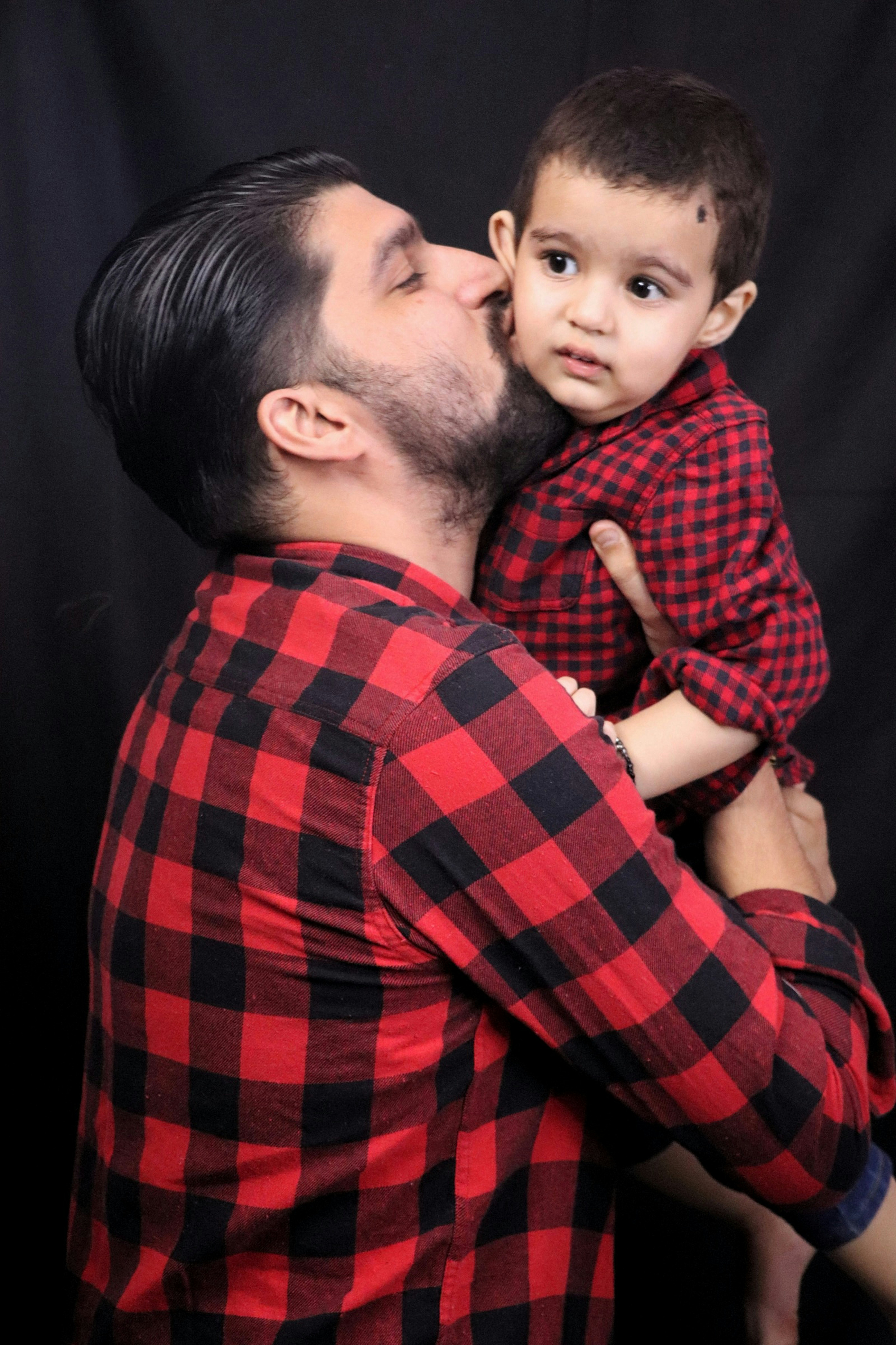 man in red and black checkered dress shirt carrying baby