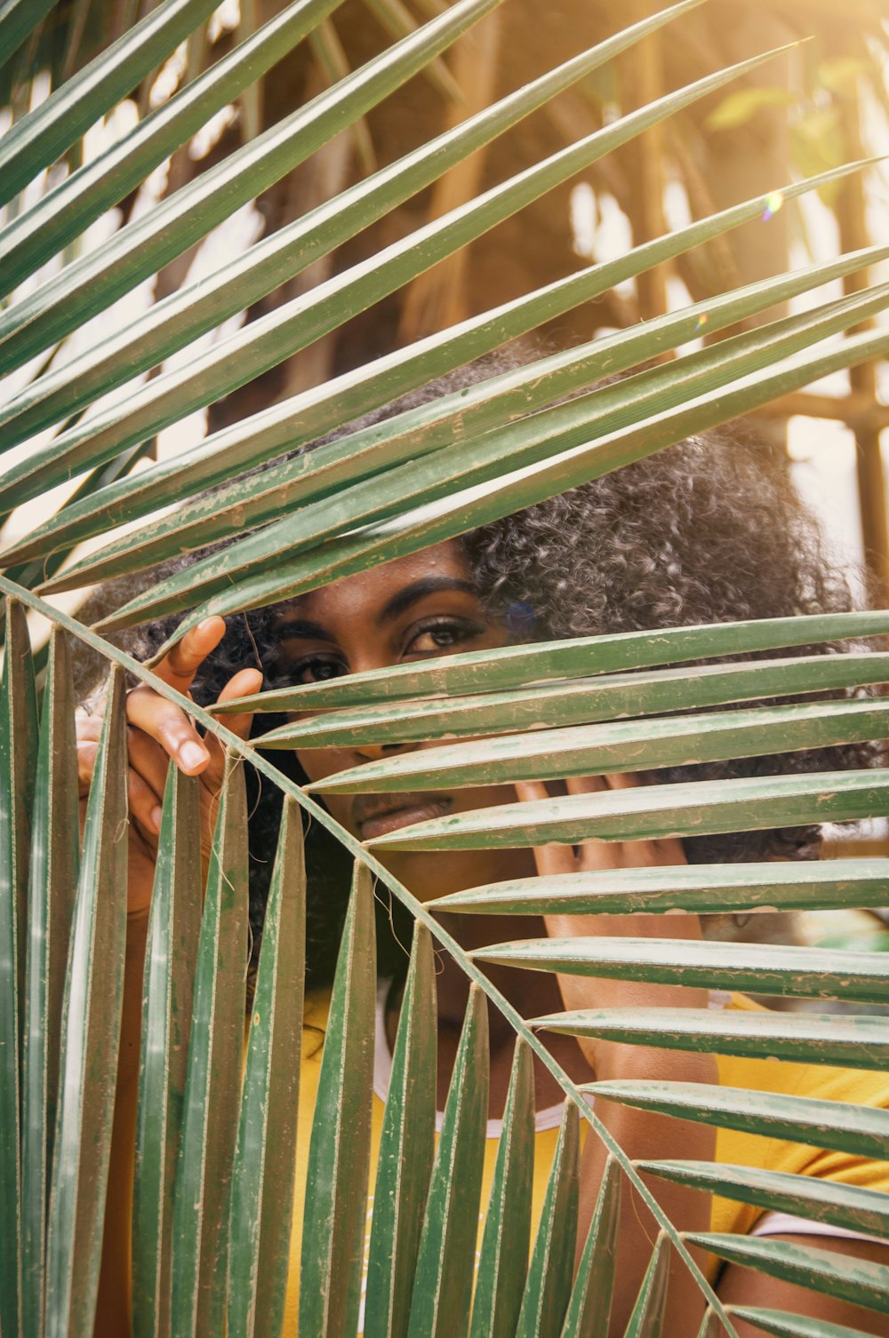 a woman hiding behind a palm leaf