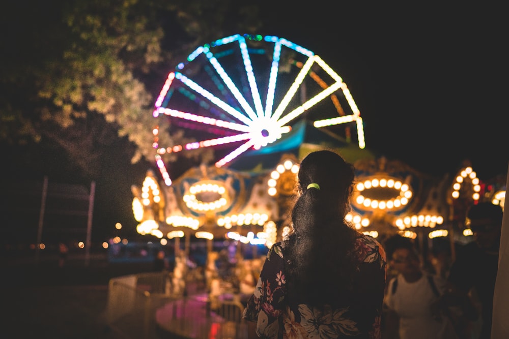 woman in black floral dress standing near ferris wheel during night time
