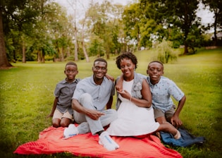 3 women and 2 men sitting on green grass field during daytime